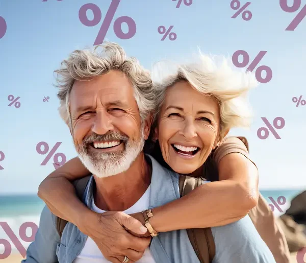 Lachendes älteres Paar am Meer umarmt sich, im Hintergrund sieht man Prozente. Angebote von Schuy Reisen.