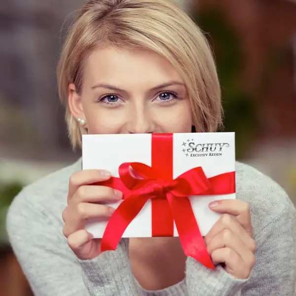 Eine junge Frau hält freudig einen Schuy Gutschein als Geschenk in ihrer Hand vor Ihr Gesicht.