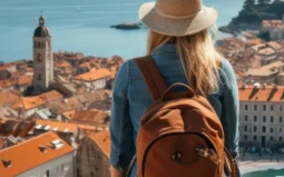 Eine junge Frau mit Rucksack blickt auf einen Urlaubsort am Meer während einer Kurz- & Erlebnisreise.
