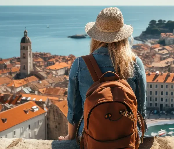 Eine junge Frau mit Rucksack blickt auf einen Urlaubsort am Meer während einer Kurz- & Erlebnisreise.