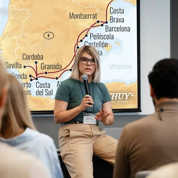 Frau mit Mikrofon vor einer Leinwand in der Wartelounge während der Schuy Reisevorträge.