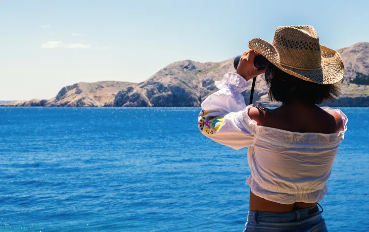 Frau schaut mit Fernglas aufs adriatische Meer