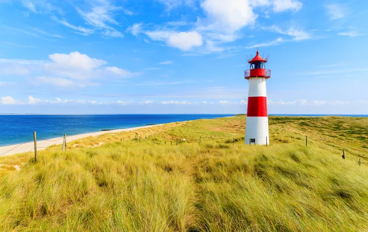 Ellenbogen lighthouse on sand dune against blue sky with white clouds on northern coast of Sylt island, Germany