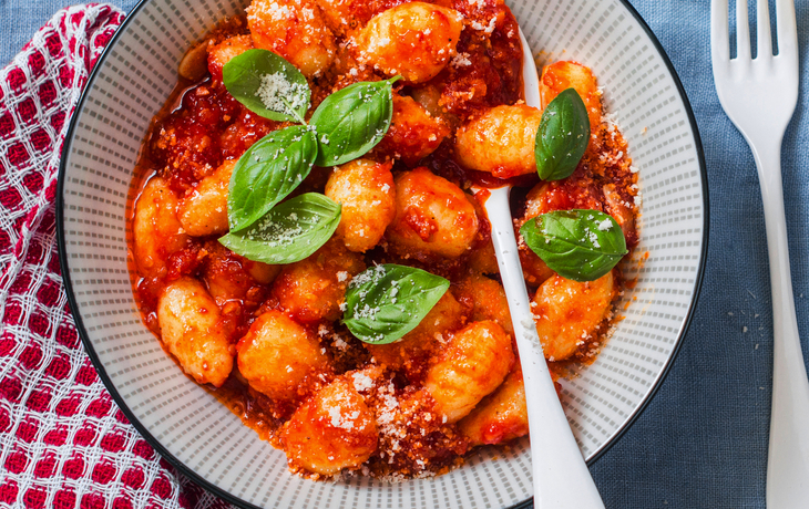 Gnocchi mit Tomatensauce, Basilikum und Parmesan auf blauem Hintergrund