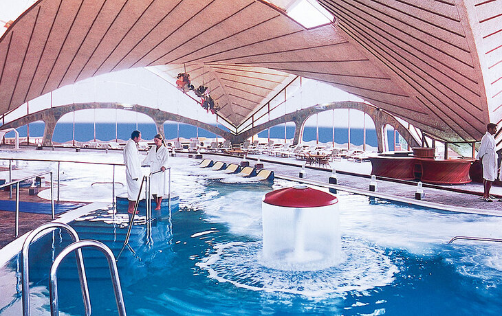 Innenansicht eines Hotelpools mit Menschen in Bademänteln und moderner Architektur.