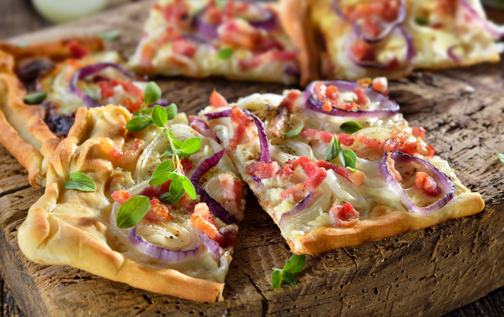 Elsässer Flammkuchen mit Zwiebeln und Speck rustikal auf altem Schneidbrett serviert