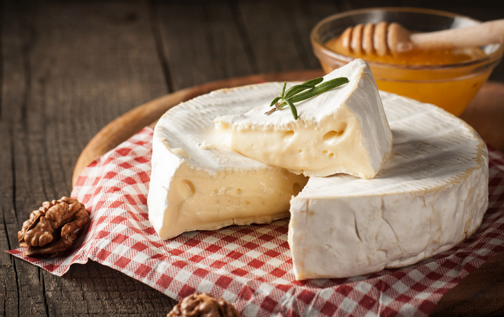 Frischer Brie-Käse auf einem Holzbrett mit Nüssen, Honig und Blättern