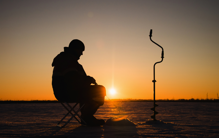 Schattenbild eines Fischers beim Wintereisfischen bei Sonnenuntergang