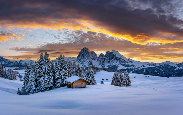 Panoramablick auf die Seiser Alm mit gemütlichen Holzhütten und Sonnenuntergangshimmel
