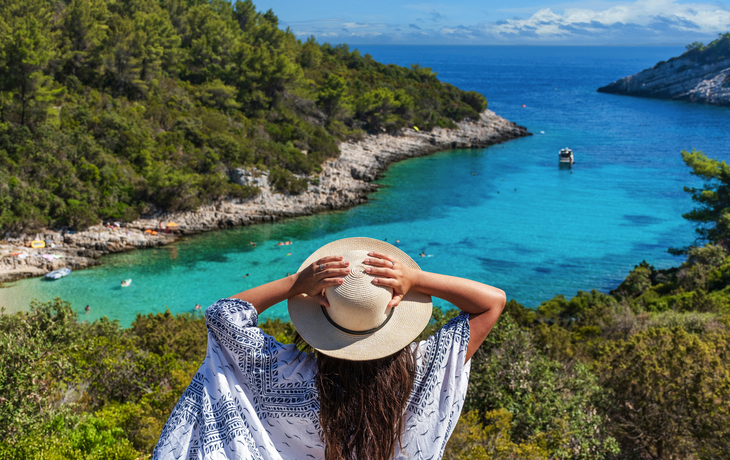 Rückansicht einer jungen Frau mit Hut, die den Strand von Zitna in Zavalatica auf Korčula, Kroatien, betrachtet