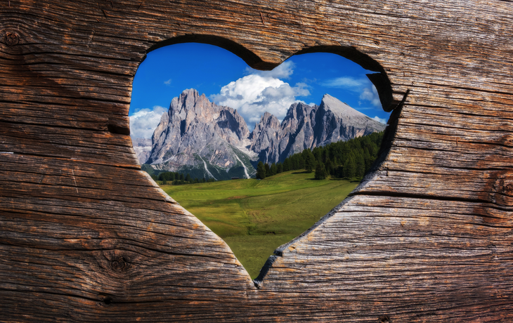 Mit lieben Grüßen aus den Dolomiten in Italien. Ein herzförmiger Blick durch die Bank auf die Berge. 