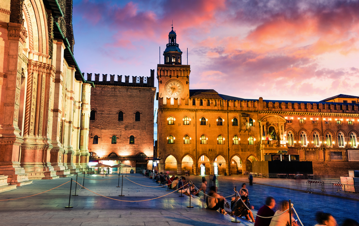 farbenfroher Frühlingssonnenuntergang auf dem Hauptplatz der Stadt Bologna mit dem Palazzo d'Accursio und der Fassade der Basilica di San Petronio