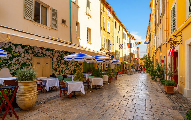 A picturesque alley of shops and sidewalk cafes in the colorful old town section of the Mediterranean resort city of Saint-Tropez, France, along the French Riviera.