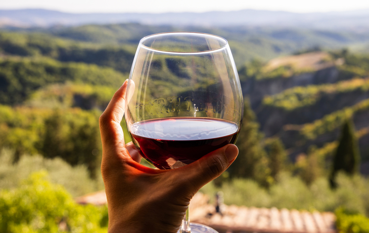 Frau hält ein Glas Rotwein in der Hand, im Hintergrund die Landschaft Italiens