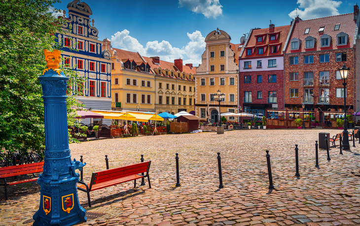 Traditionelle blaue Wasserpumpe mit dem Greifenkopf aus dem Stadtwappen von Stettin und dem Altstädter Ring im Hintergrund. 