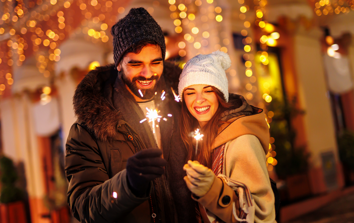 Paar, das auf den Straßen der Stadt ausgelassen Silvester feiert und mit Wunderkerzen winkt