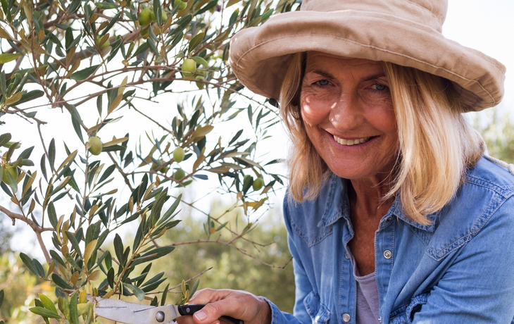 Porträt einer glücklichen Frau, die einen Olivenbaum auf einem Bauernhof beschneidet