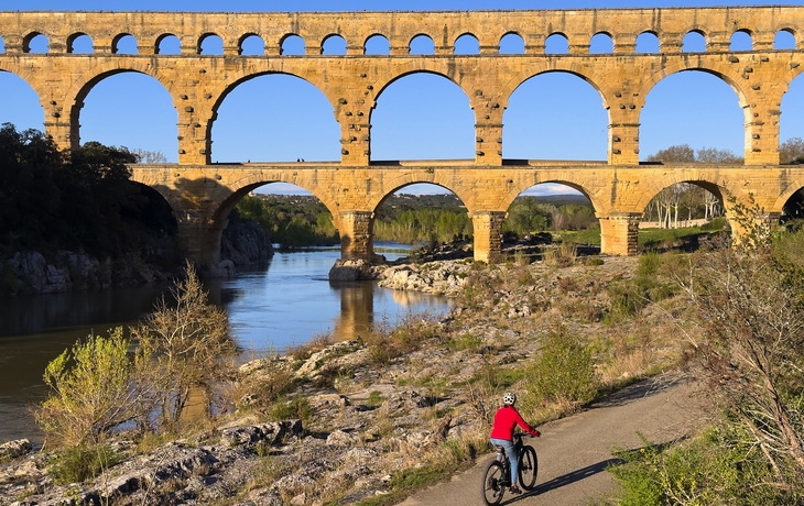 ältere Frau beim Mountainbiken mit ihrem E-Bike unterhalb des berühmten römischen Aquädukts Pont du Gard