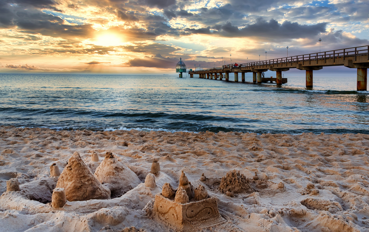 Tauchgondel und Strand mit Sandburgen im Vordergrund in Zinnowitz bei Sonnenuntergang. 