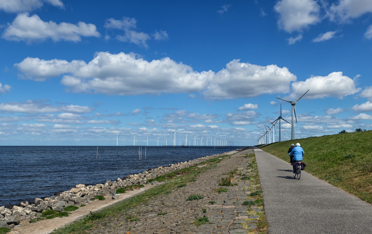 Nnederländischer Deich am IJsselmeer mit älteren Radfahrern und Windkraftanlagen